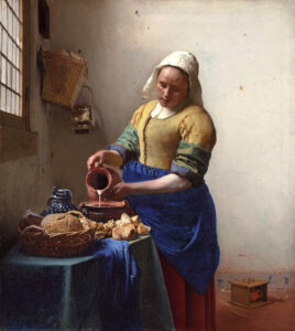 detail from Vermeer's The Milkmaid: woman in white headscarf, blue apron pours milk from clay jug into bowl